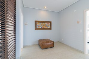 A hallway with a wooden slatted wall, a framed fish artwork, a brown leather ottoman, and a door labeled 'Suite Toquinho'. - Mansão Carneiros By Carpediem (Tamandaré)