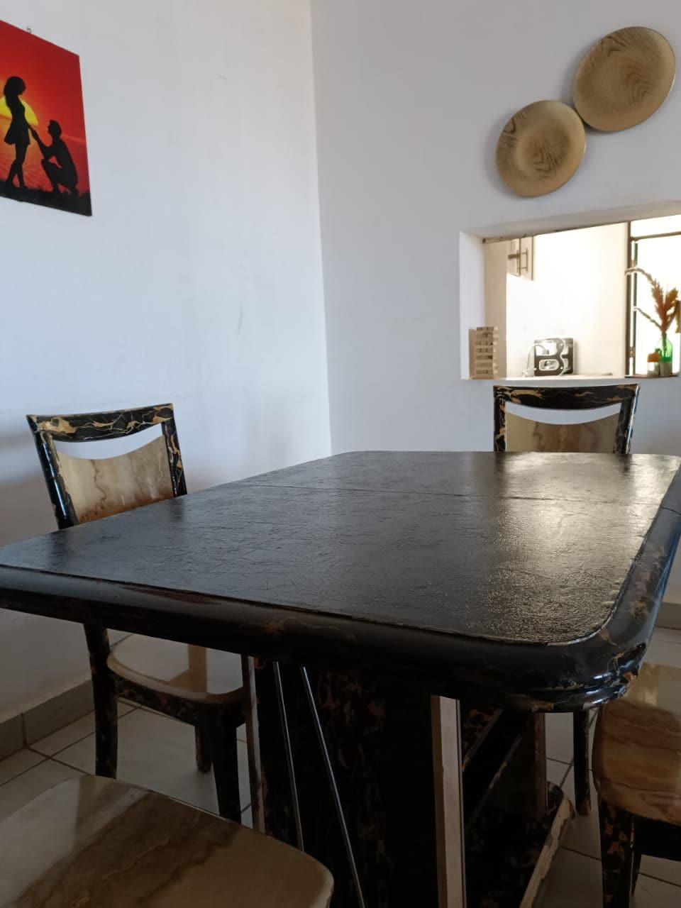 Un coin repas comprenant une table rectangulaire, deux chaises recouvertes d’un tissu à motifs et une assiette décorative fixée au mur.
