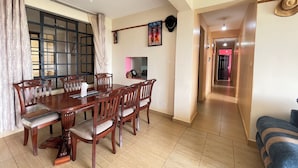 A dining area with a wooden table and chairs, a window with curtains, a wall-mounted picture, and a hallway leading to another room.