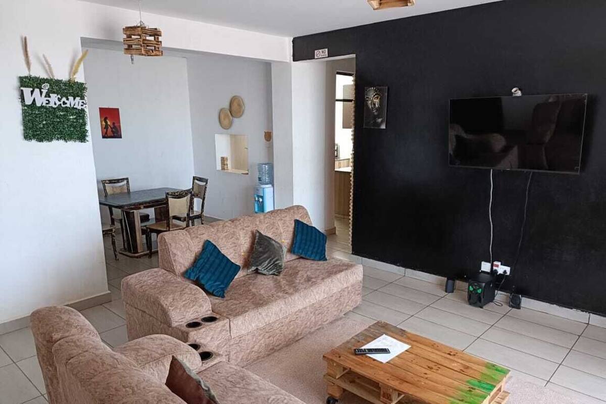 Una sala de estar con un sofá color beige, una mesa de centro de madera y un televisor montado en una pared negra.