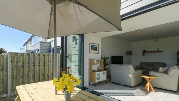 A patio with a wooden table and a vase of yellow flowers, a white sofa, and a TV in a living room. - 6 Gwel Yr Wyddfa (Ty Croes)