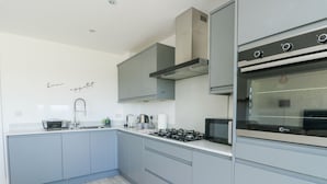 A modern kitchen with grey cabinets, a built-in stove, and a microwave. - 6 Gwel Yr Wyddfa (Ty Croes)