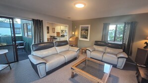 A living room with two leather sofas, a glass coffee table, and a dining area with a table and chairs. - Esplanade Townhouse  (Gisborne)