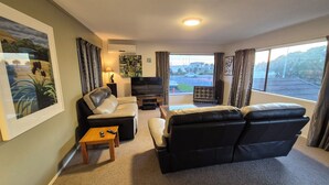 A living room with a sofa, a chair, a TV, and a window with a view of buildings. - Esplanade Townhouse  (Gisborne)