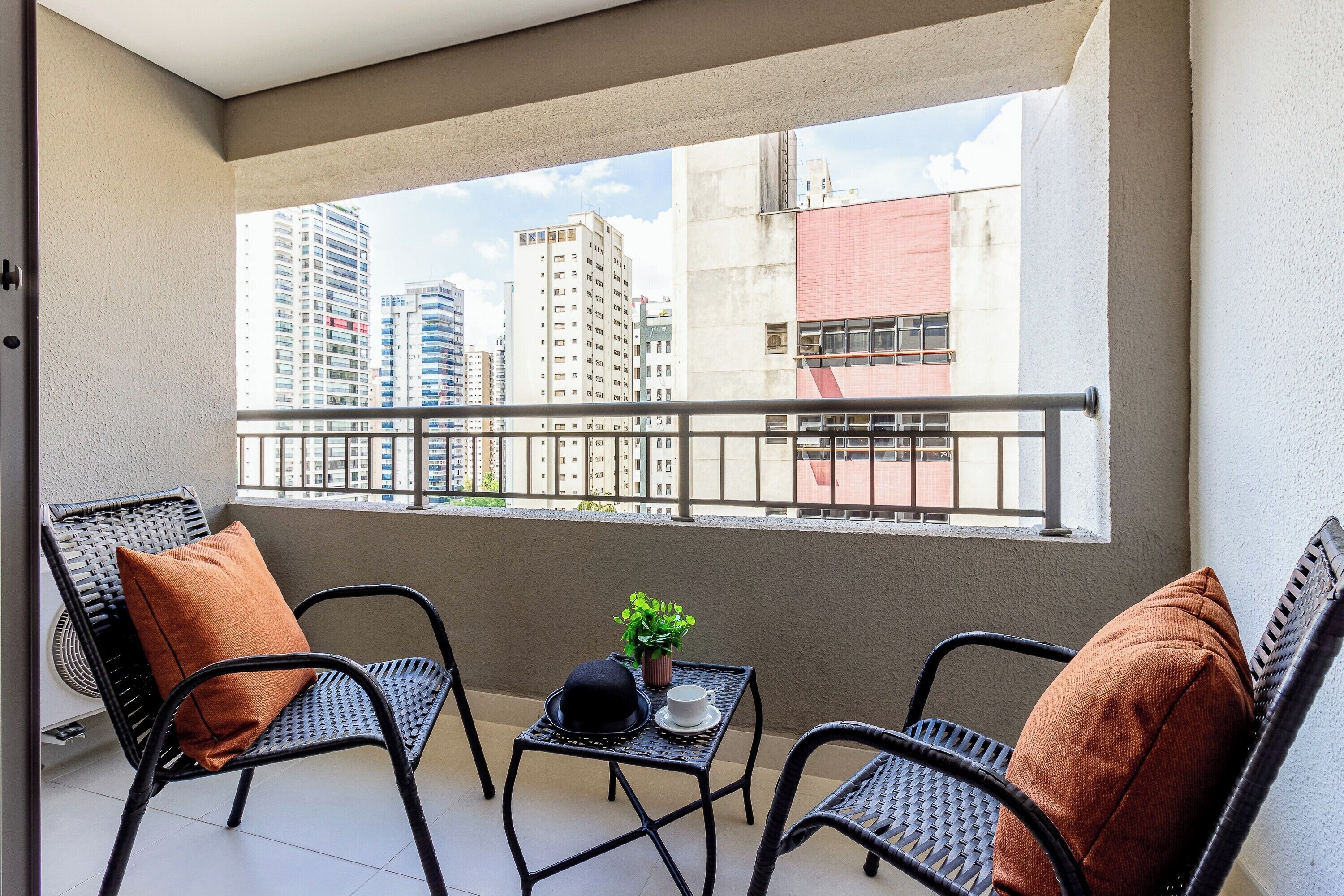 Ein Balkon mit zwei Korbstühlen, einem kleinen Tisch und einem Blumentopf.