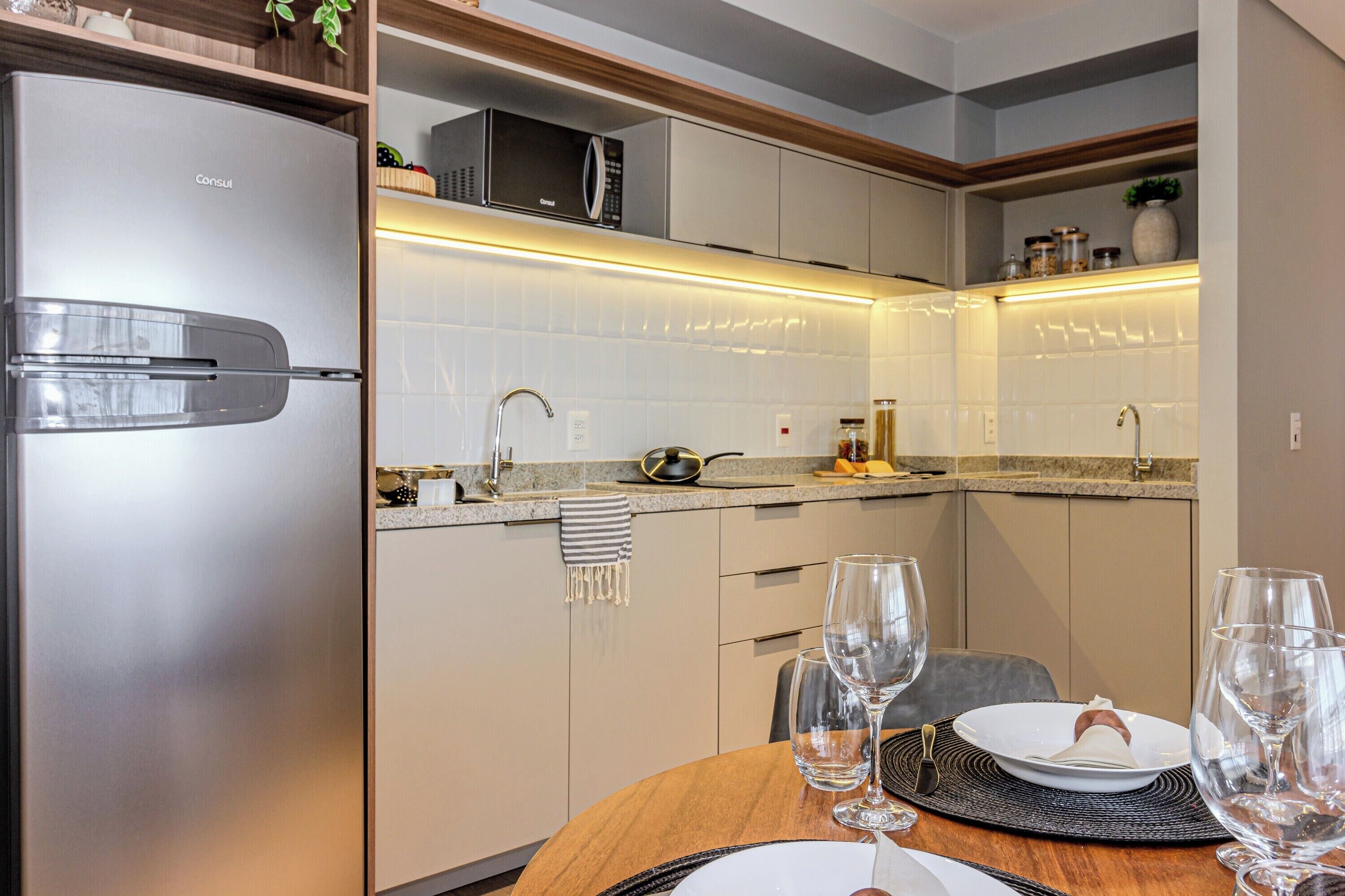 A modern kitchen with a stainless steel refrigerator, a microwave, and a sink. There are wine glasses on the table, suggesting a dining area.