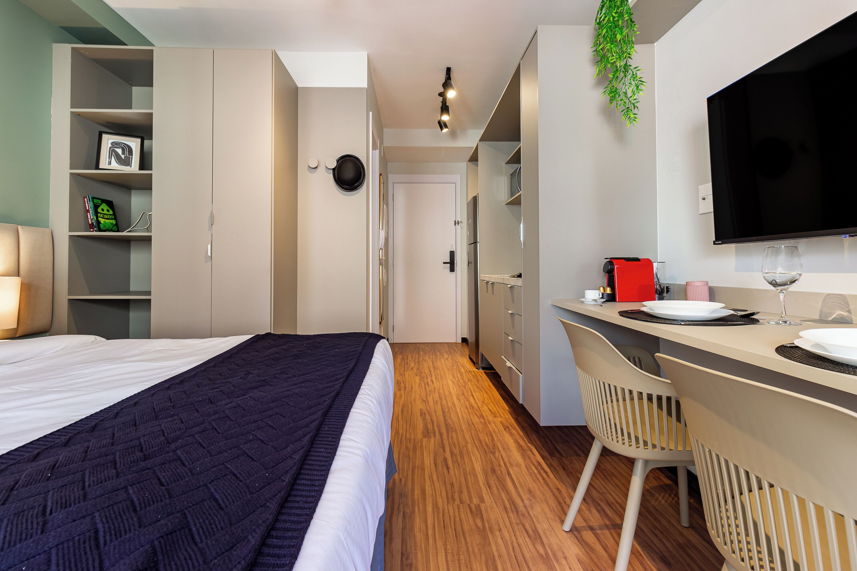 Una habitación de hotel moderna con una cama, un escritorio con silla, un televisor y una estantería.