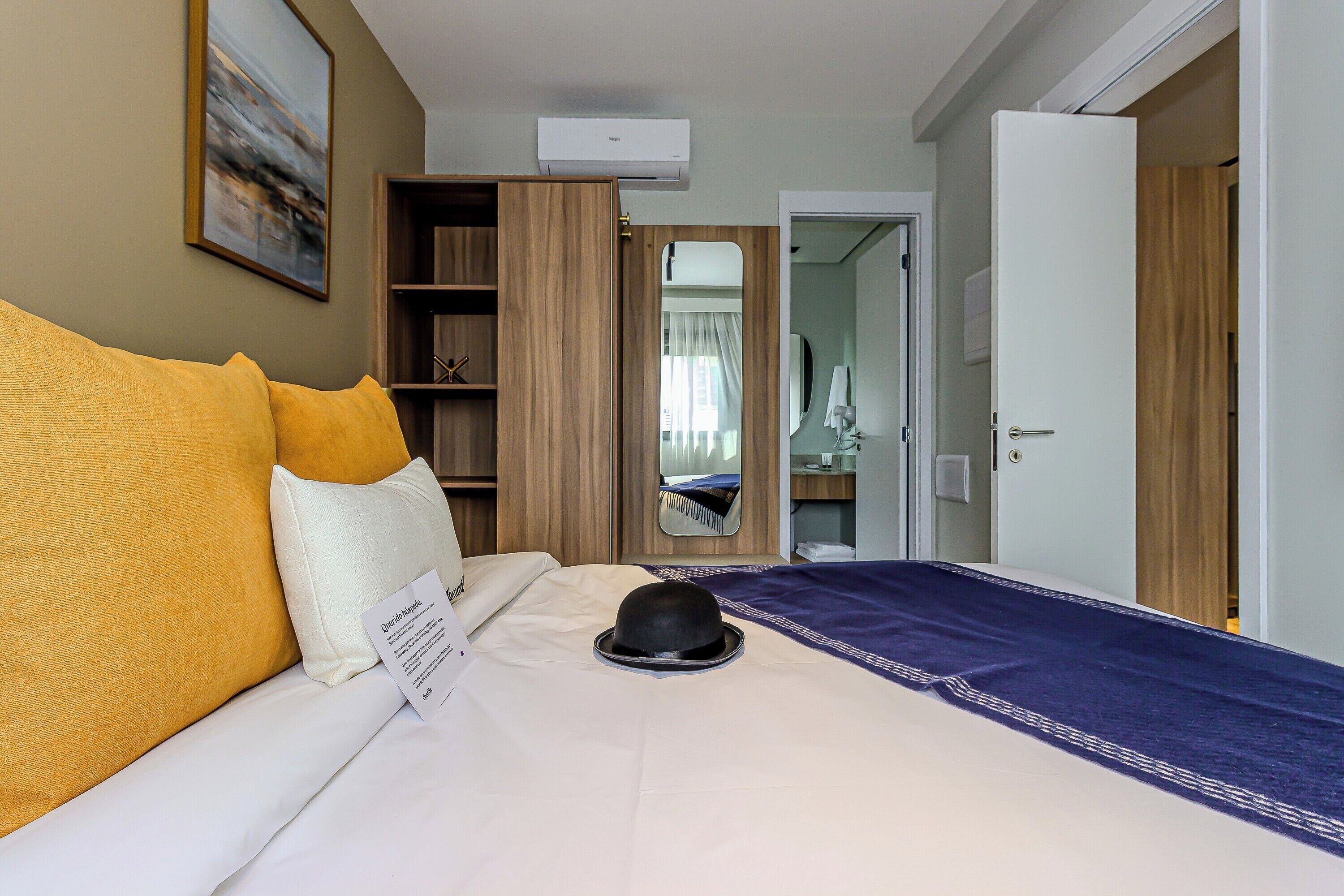 A hotel room with a bed, a wardrobe, a mirror, and an air conditioning unit.