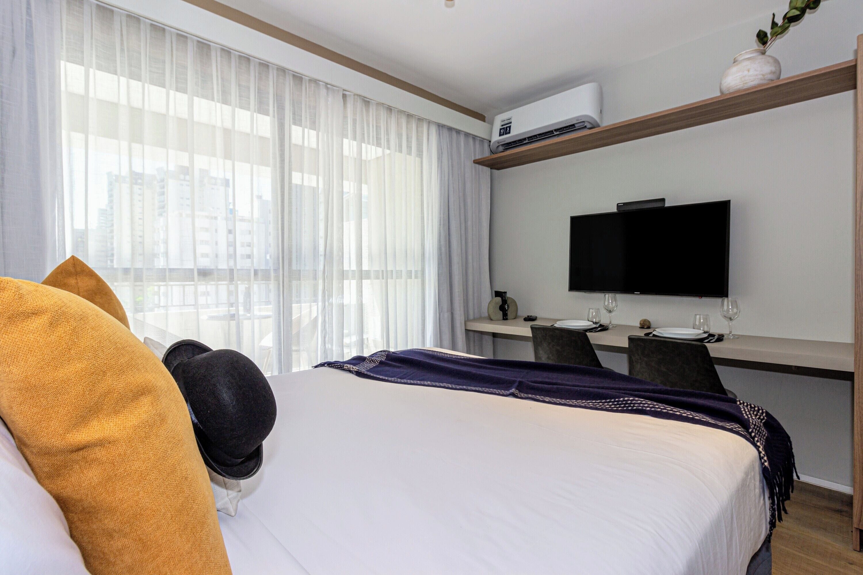 Una habitación de hotel con cama, escritorio, televisión y ventana con cortinas.