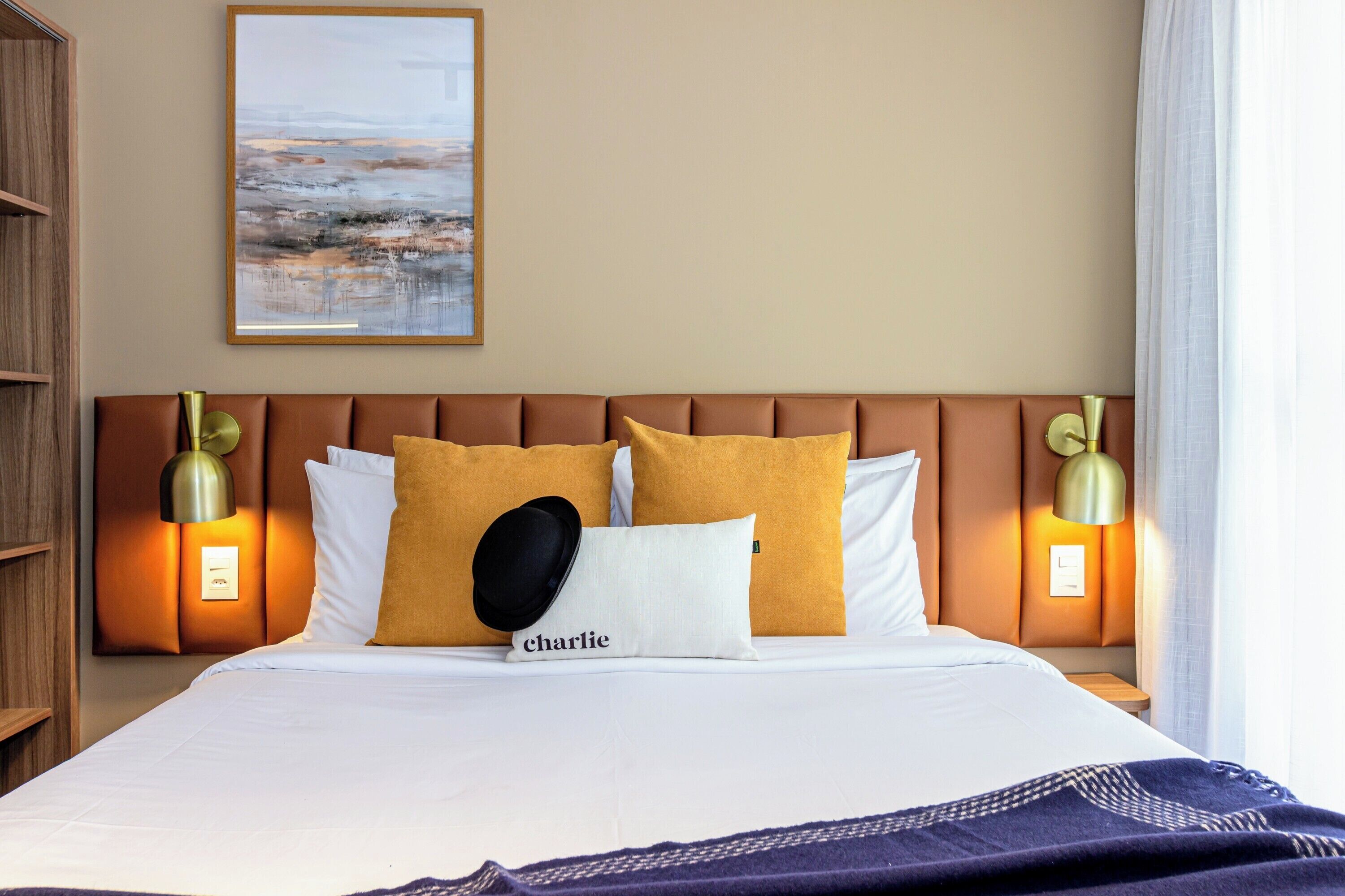 A neatly made bed with a headboard, two bedside lamps, and a framed artwork above.