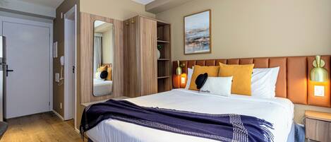 Une chambre d’hôtel moderne avec un grand lit, une armoire, une table de chevet et une petite table à côté du lit.