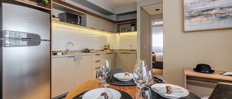 A modern kitchen with a built-in refrigerator, microwave, and wooden cabinets. There is a dining table set with plates, glasses, and cutlery.
