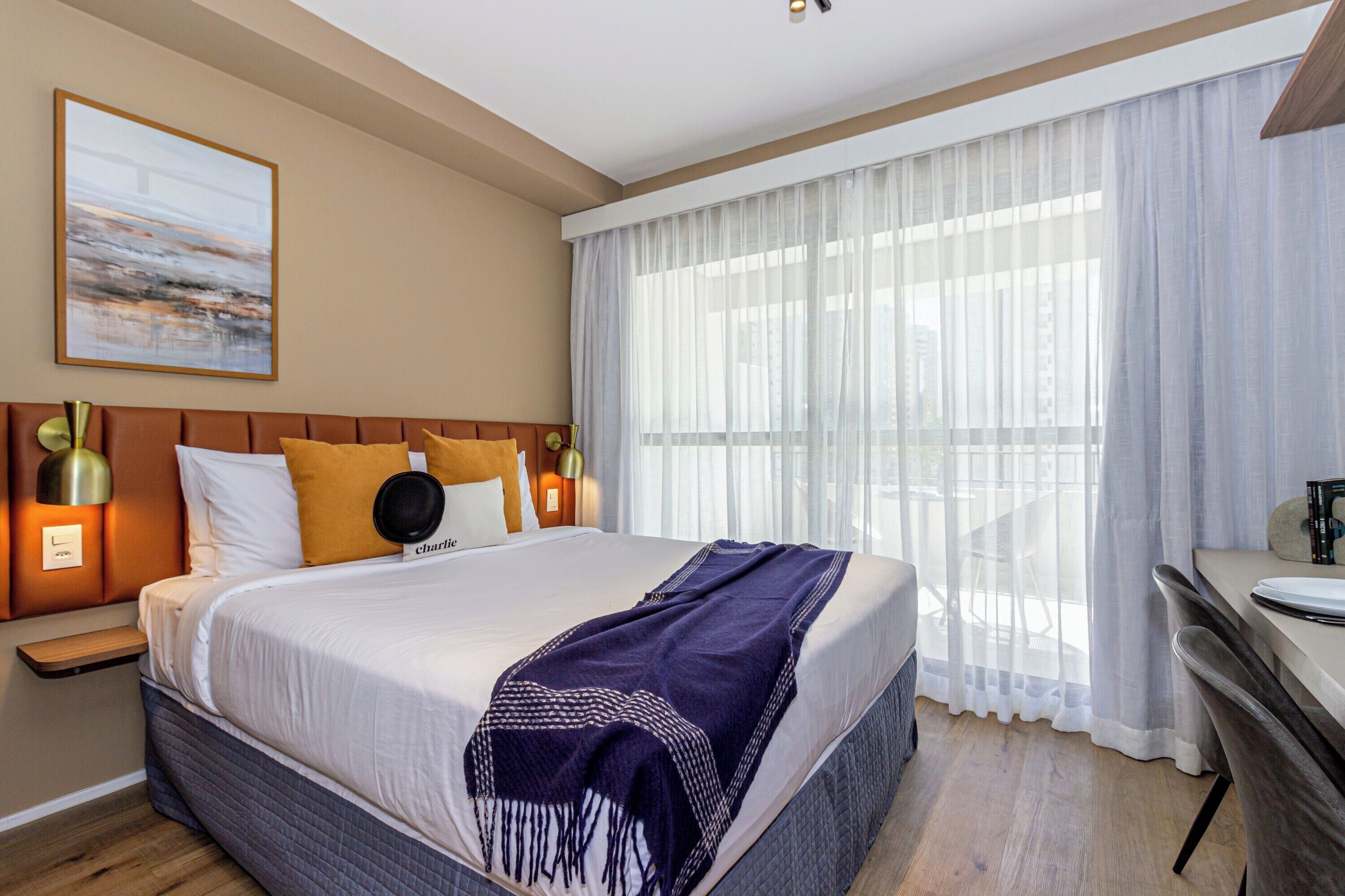 Ett hotellrum med en stor säng, ett skrivbord och utsikt över omgivningarna genom tunna gardiner.
