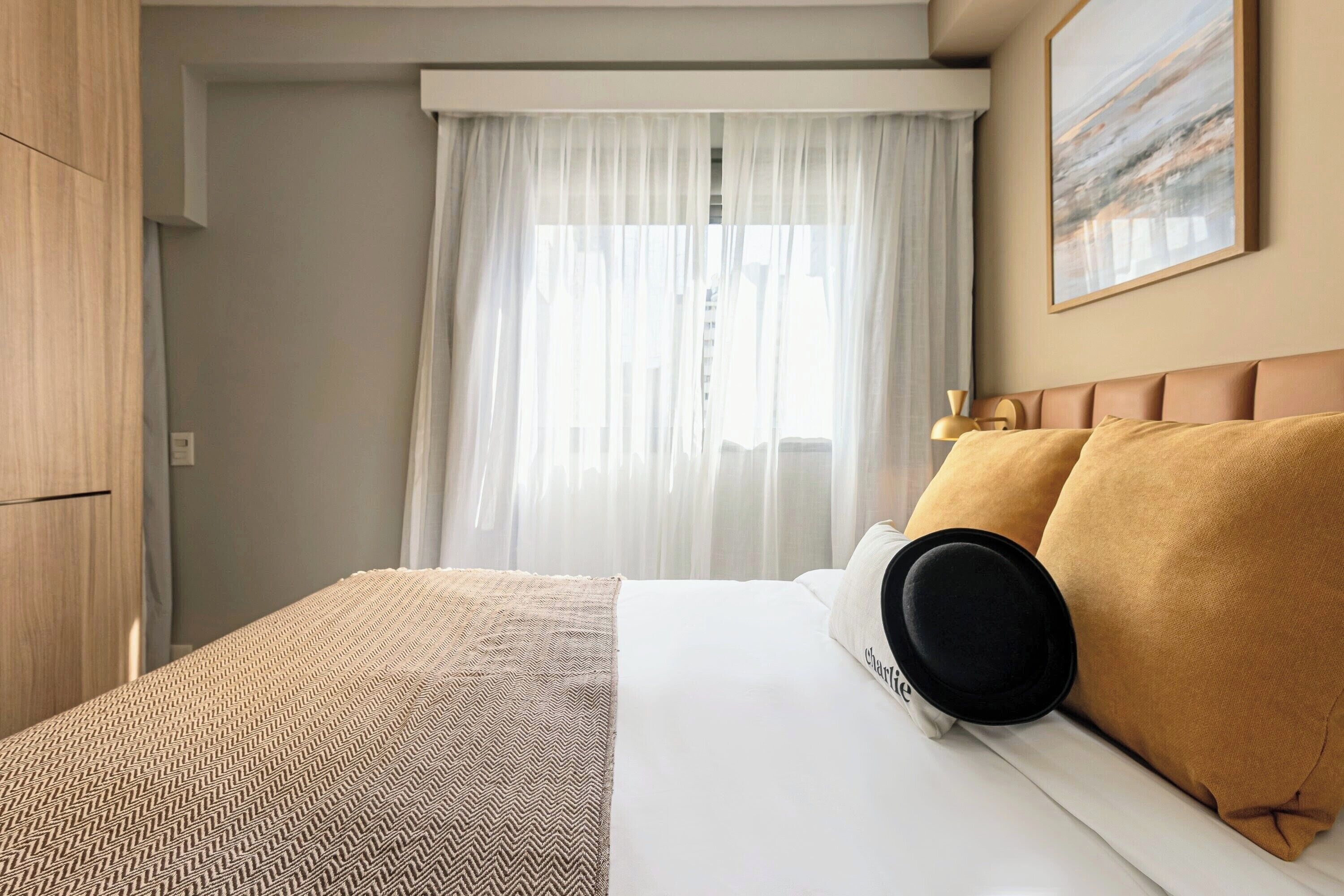 Ein Hotelzimmer mit Bett, Kleiderschrank, einem Fenster mit Vorhängen und einem Bild an der Wand.