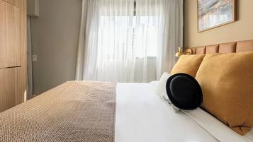 Ein Hotelzimmer mit Bett, Kleiderschrank, einem Fenster mit Vorhängen und einem Bild an der Wand.