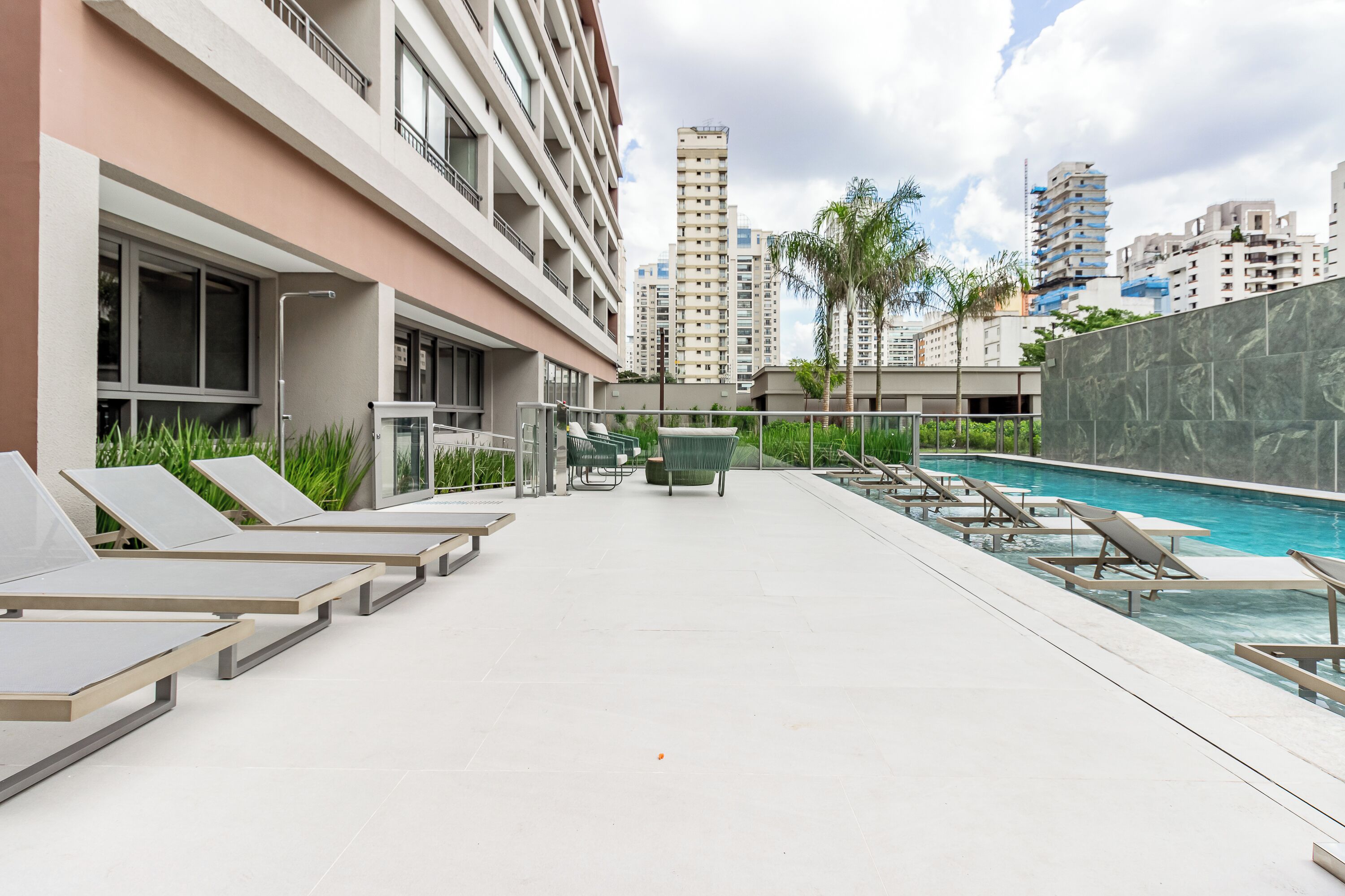 A rooftop pool area with lounge chairs, a water feature, and high-rise buildings in the background.