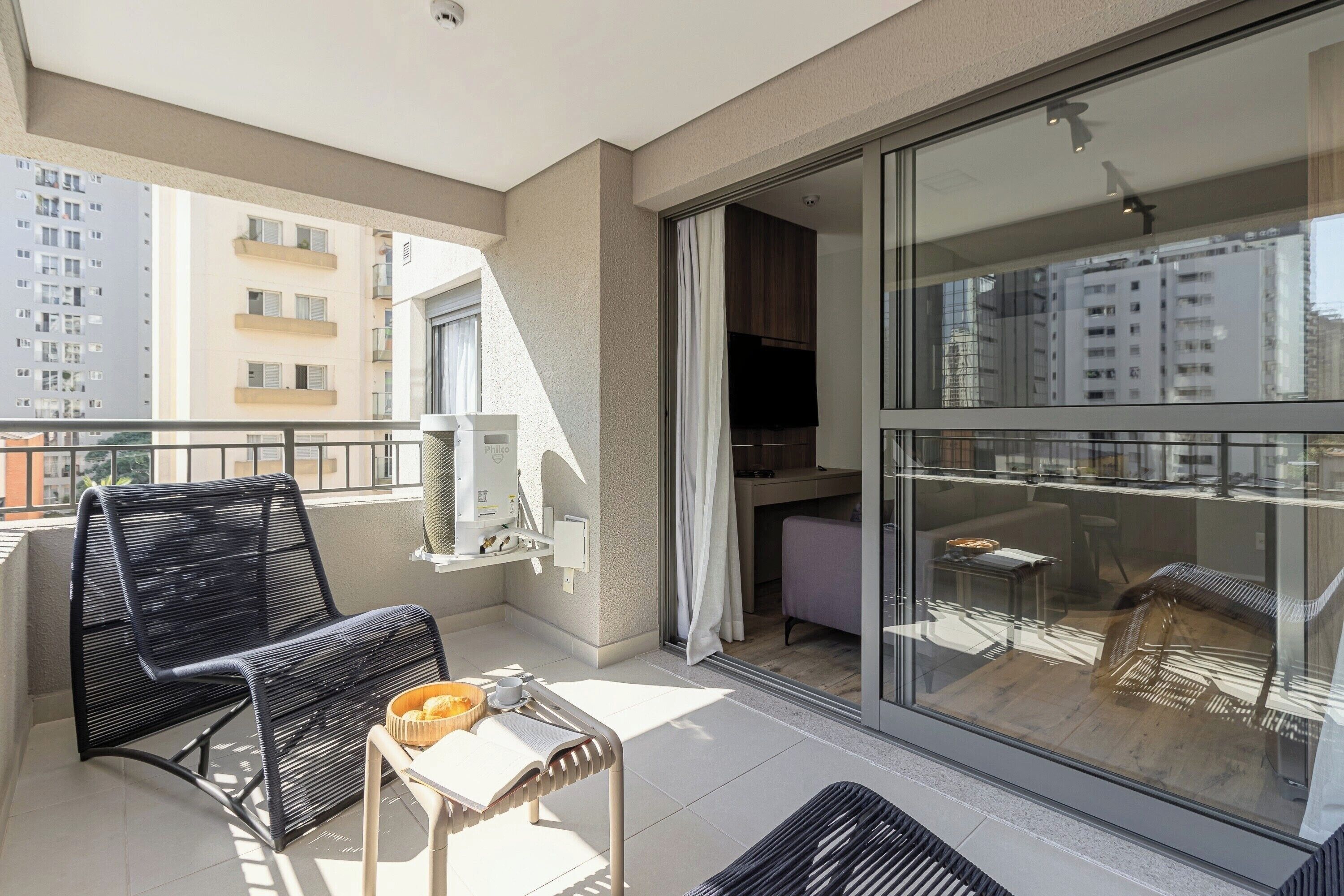 A balcony with a chair, a small table, and a window overlooking a cityscape.