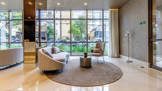 A modern lobby with a large glass window, two sofas, a small round table, and a floor lamp. - Charlie Grand Vitrali Moema (São Paulo)