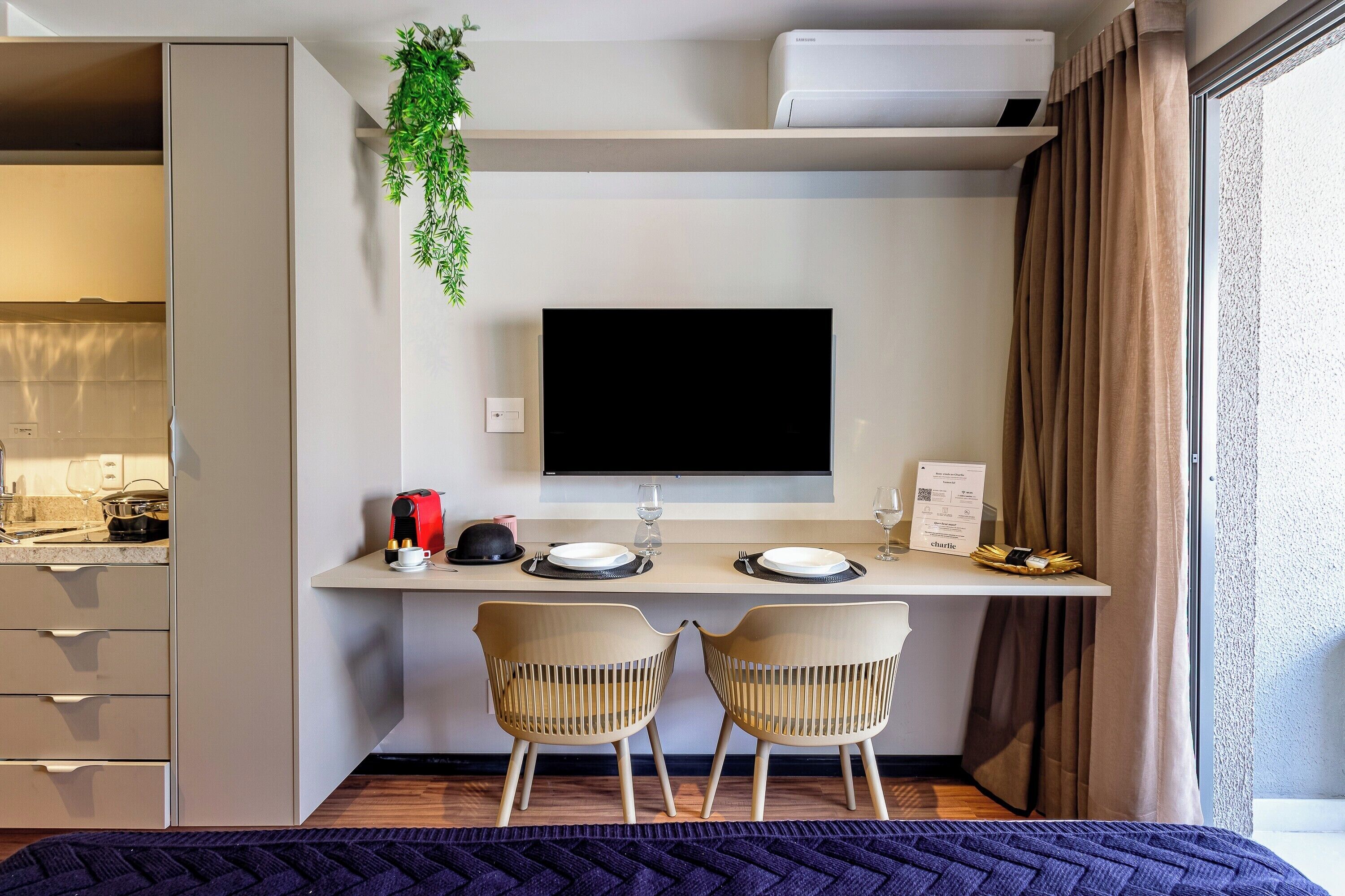 Ein modernes Zimmer mit einem Bett, einem Schreibtisch mit Flachbildfernseher, zwei Stühlen und einem Fenster mit Vorhängen.