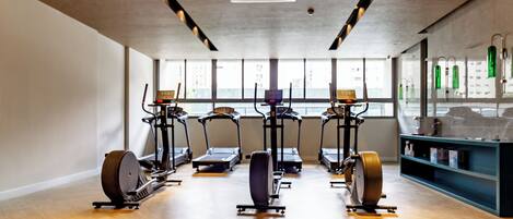 Un gimnasio con equipo de ejercicio, amplias ventanas y suelo de madera.