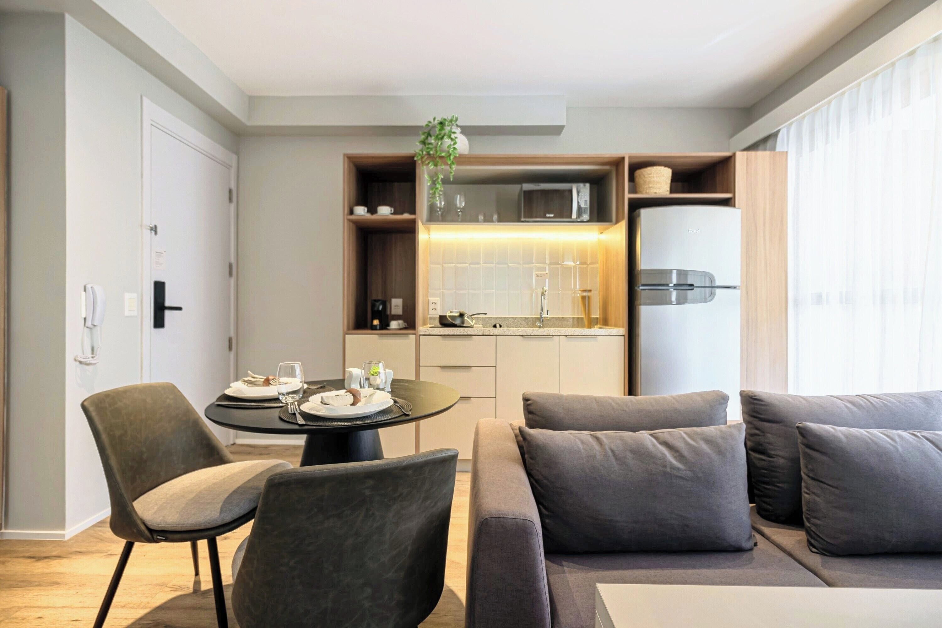 A modern living room with a sofa, chairs, a dining table, and a kitchen area with a refrigerator and microwave.