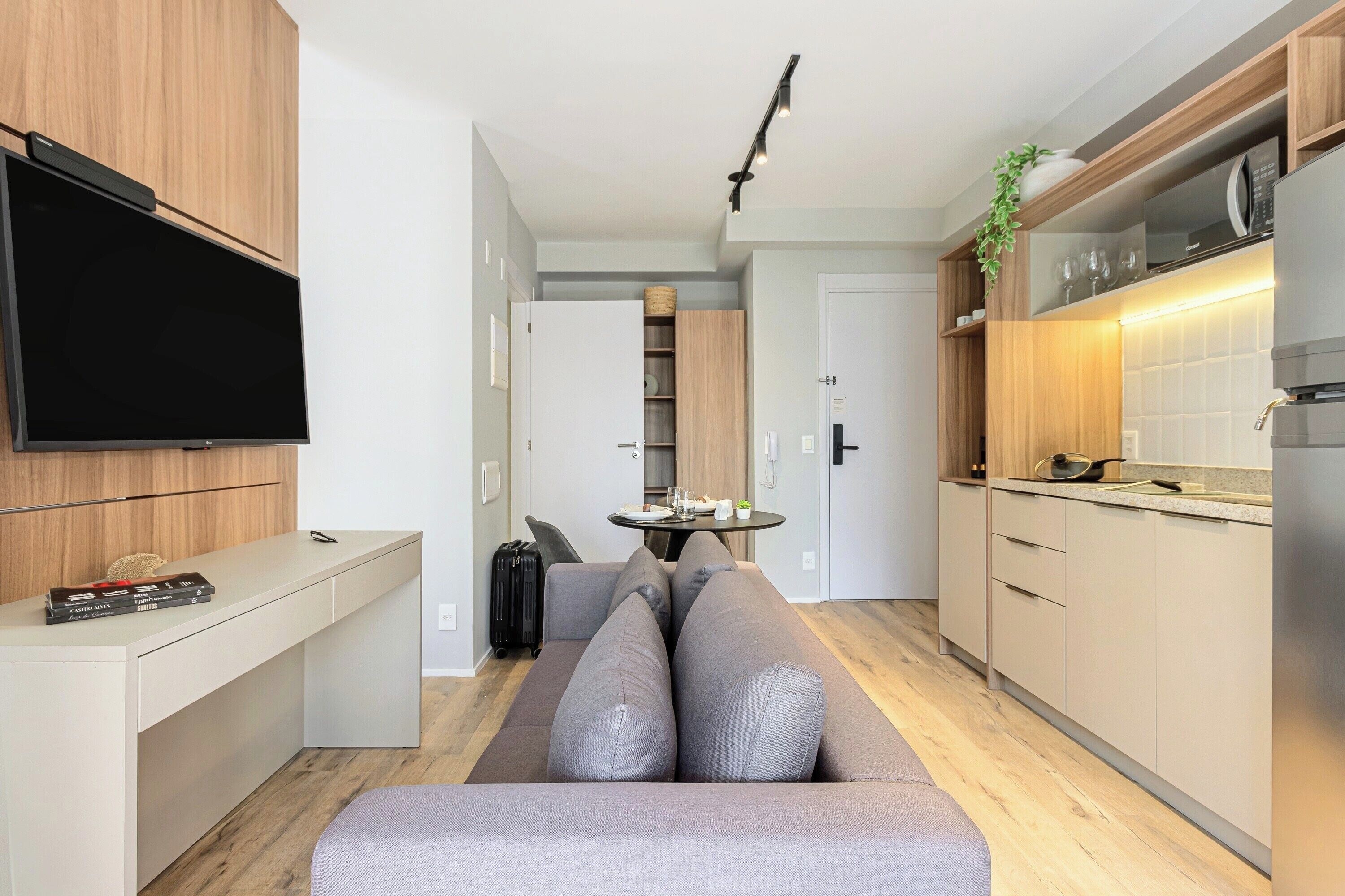 Una cocina moderna con microondas integrado, una zona de comedor con mesa y sillas, y un  área de estar con sofá y cojines.