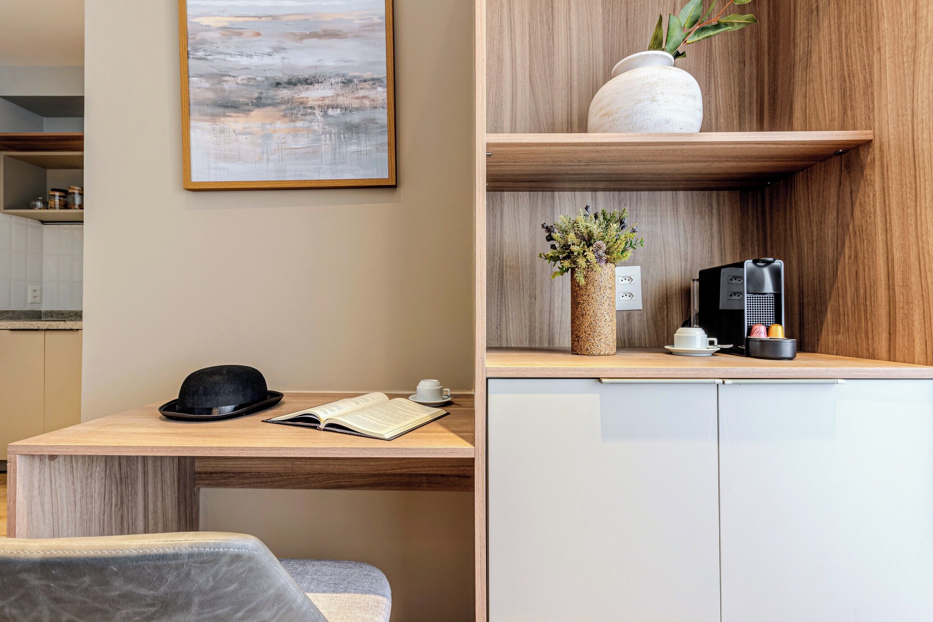 A modern kitchen with a wooden countertop, a coffee machine, a vase with flowers, and a framed picture on the wall.