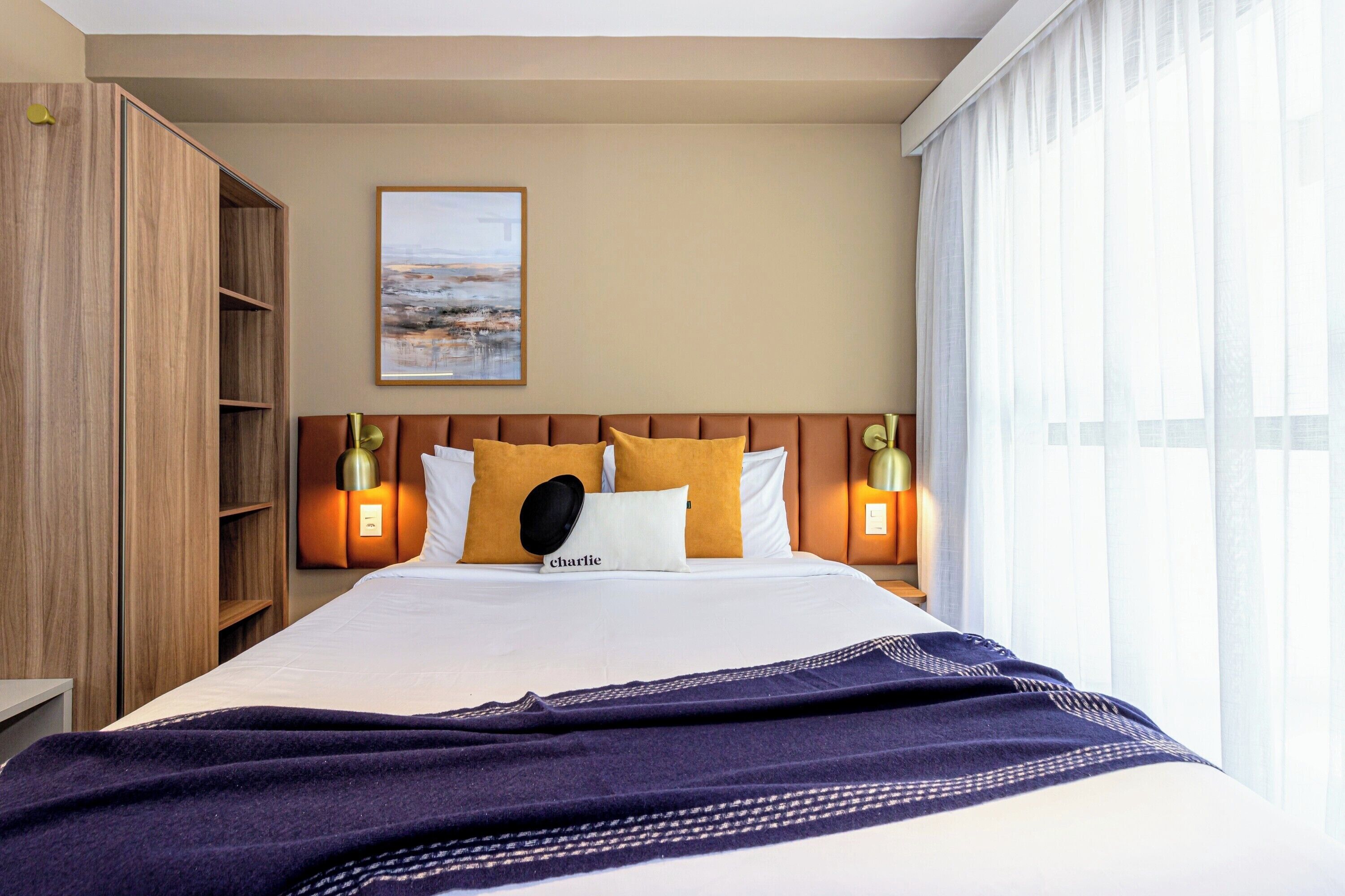 Una habitación de hotel con una cama grande, un armario, un cuadro en la pared y dos lámparas de noche.