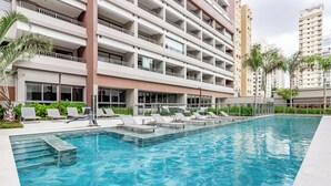 A swimming pool with lounge chairs and a building with multiple balconies in the background. - Charlie Grand Vitrali Moema (São Paulo)
