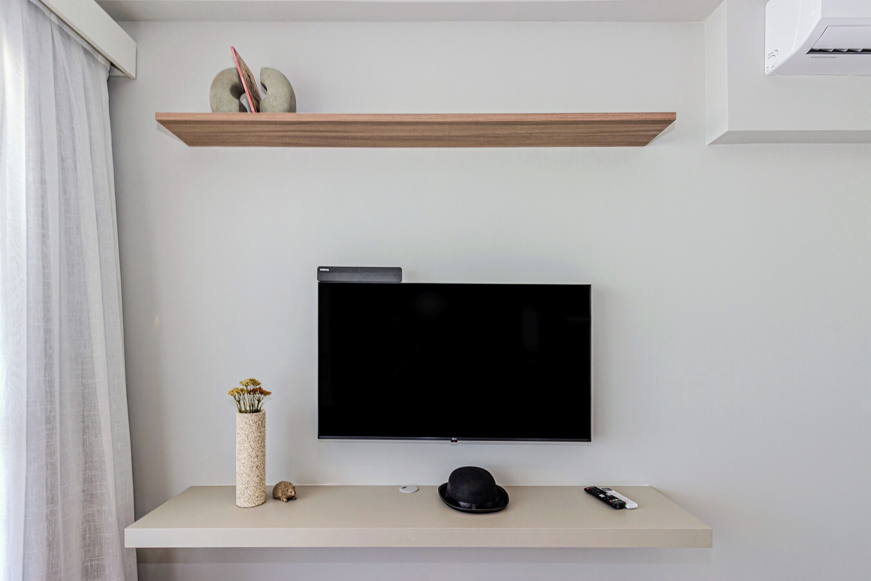 Un téléviseur à écran plat fixé au mur, avec une étagère au-dessus.