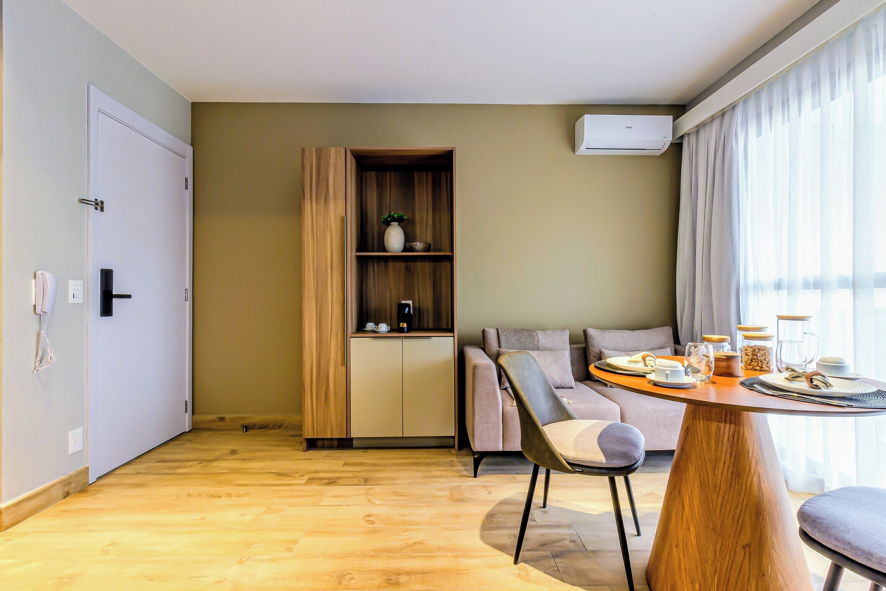 Un salon moderne avec un plancher en bois, un canapé, une table à manger avec des chaises, un meuble avec des étagères et une grande fenêtre avec des rideaux.