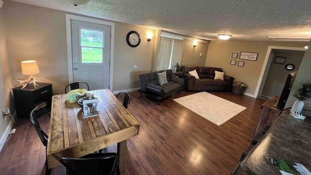 Una sala de estar con una mesa de comedor de madera, dos sofás, un tapete y una puerta con ventanal.