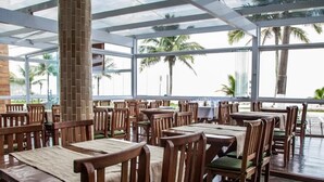 A restaurant with wooden tables and chairs, large windows, and a view of palm trees.