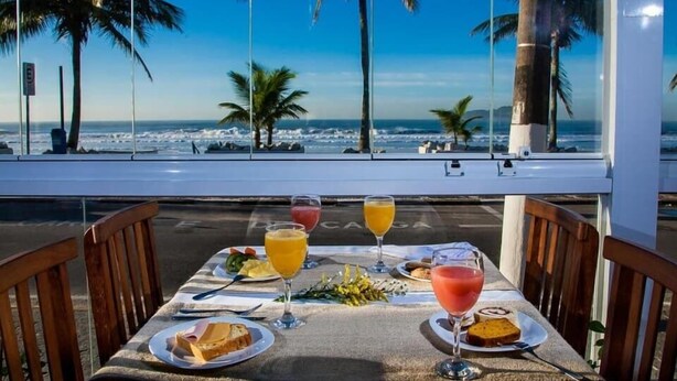 A table set with food and drinks, overlooking a beach with palm trees and the ocean.
