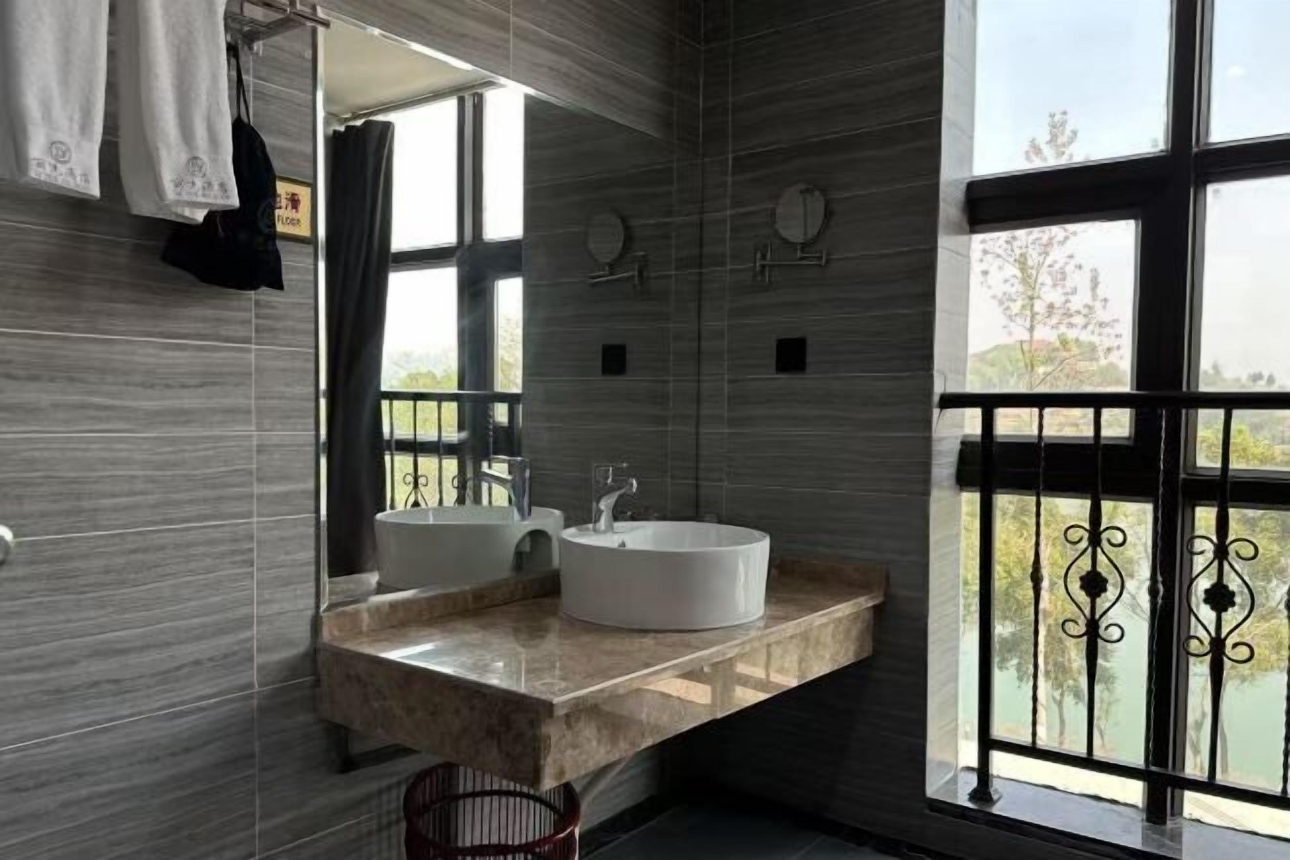 A bathroom with two sinks, a large mirror, and a window with a view of greenery.