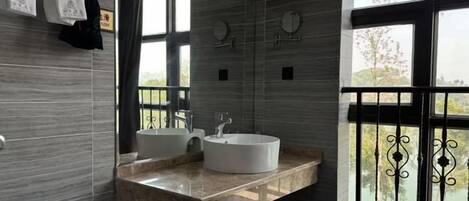 A bathroom with two sinks, a large mirror, and a window with a view of greenery.