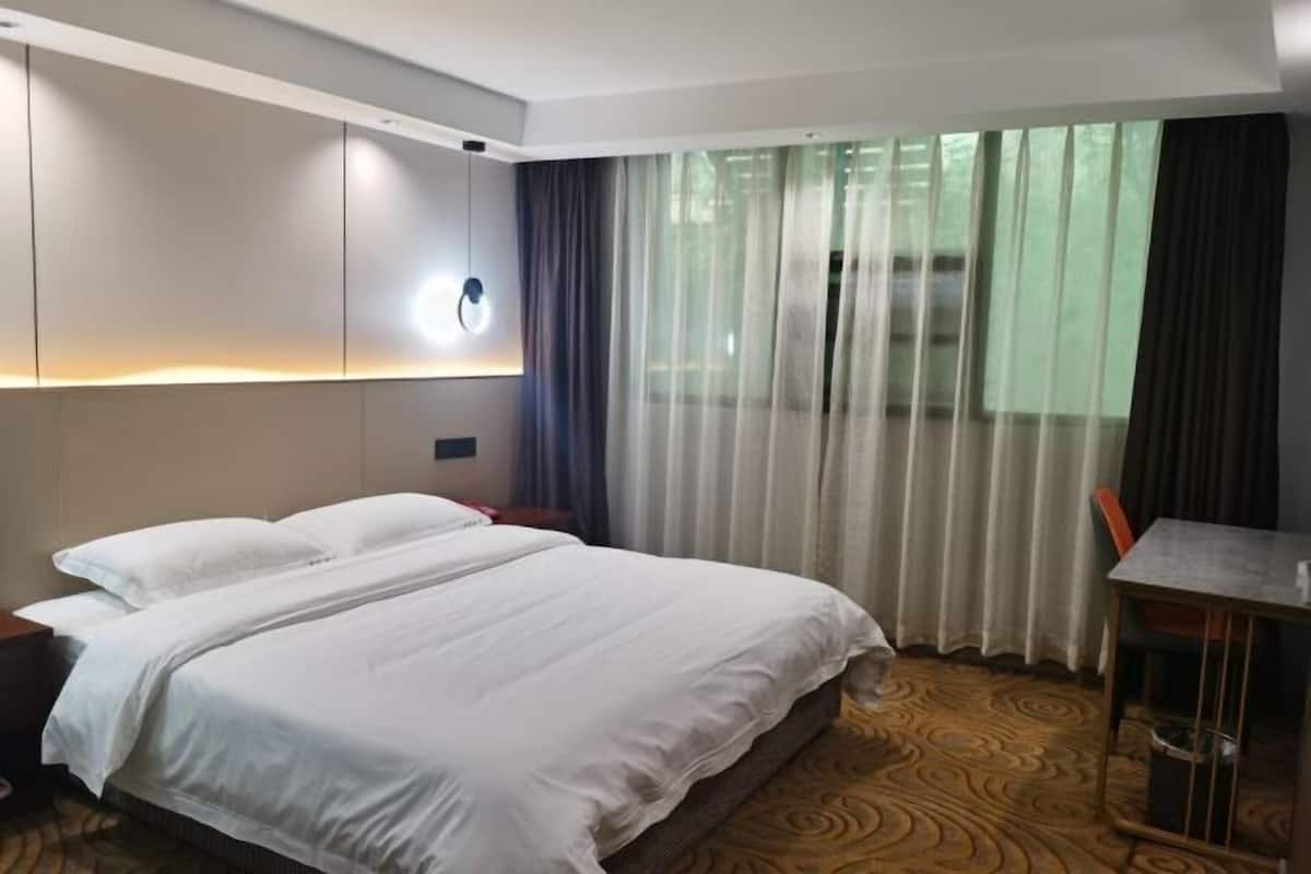 A hotel room with a bed, a desk, and a view through sheer curtains.