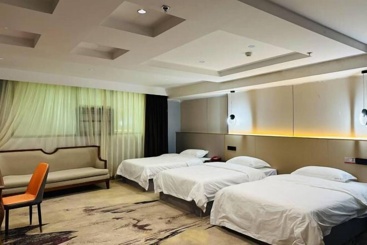A hotel room with a sofa, two beds, a headboard, and a carpet.