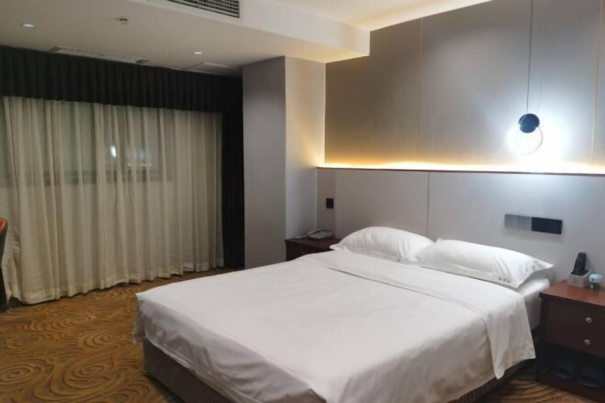 A hotel room with a large bed, a bedside table, a nightstand, and a wall-mounted light fixture.