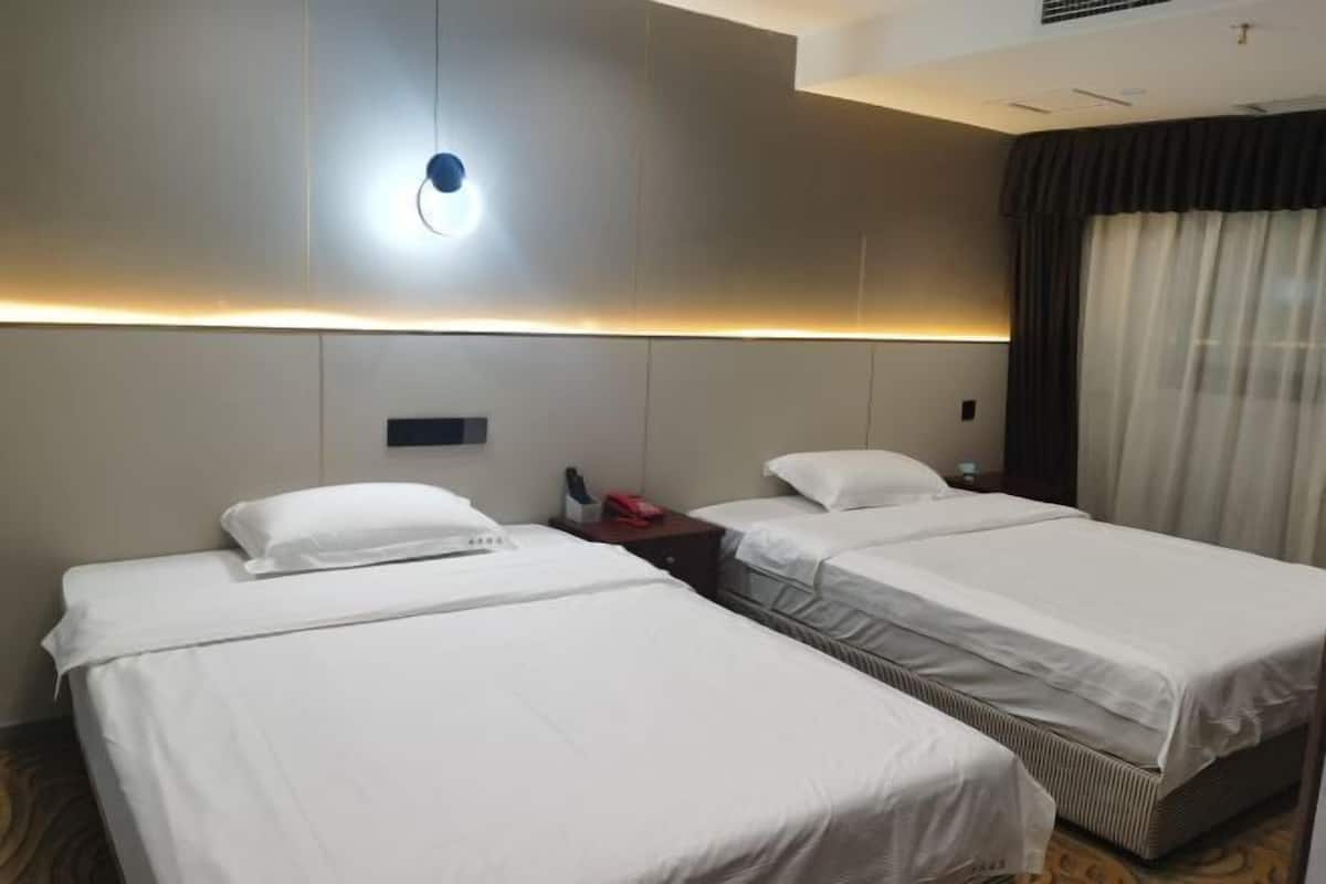 A hotel room with two single beds, a bedside table with a lamp, and a large window with curtains.