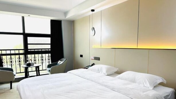 A hotel room with a large bed, a small table, two chairs, and a balcony with a railing. - Jialing Bandao Hotel (Wusheng)