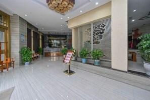 Un vestíbulo de hotel con mostrador de recepción, zona de estar y plantas en macetas.