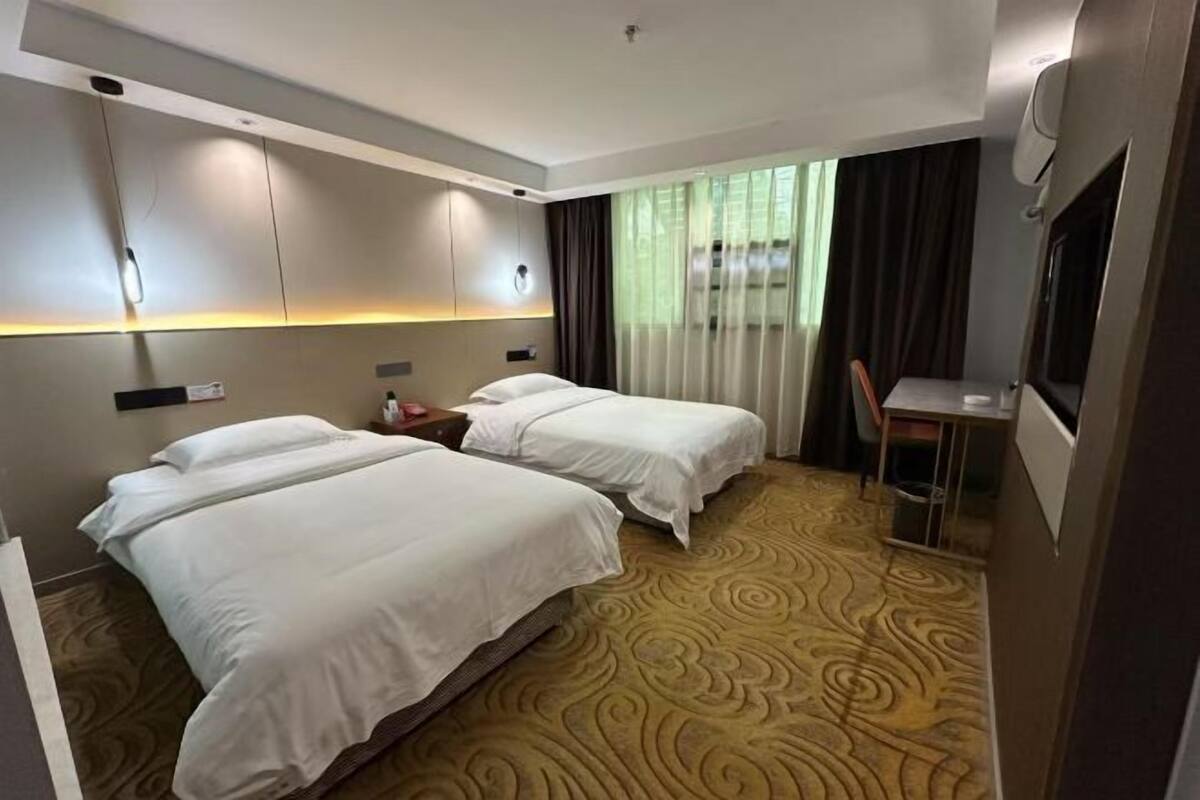 A hotel room with two beds, a desk, a chair, a TV, and a patterned carpet.