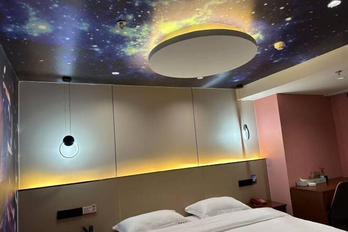 A hotel room with a bed, a desk, and a wall with a galaxy-themed ceiling.