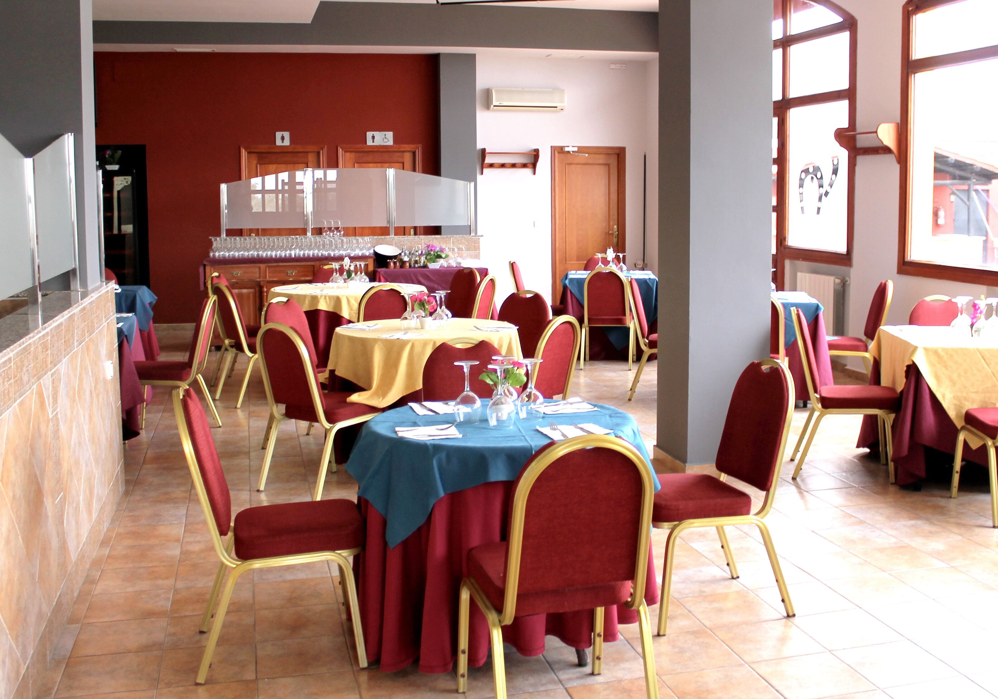 A dining area with multiple round tables, each with a blue tablecloth and red chairs.