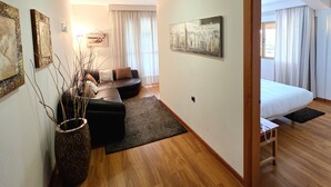 A modern hotel room with a wooden floor, a sofa, a bed, and a large window with curtains. - Hotel Los Barruecos by Croma (Malpartida de Cáceres)