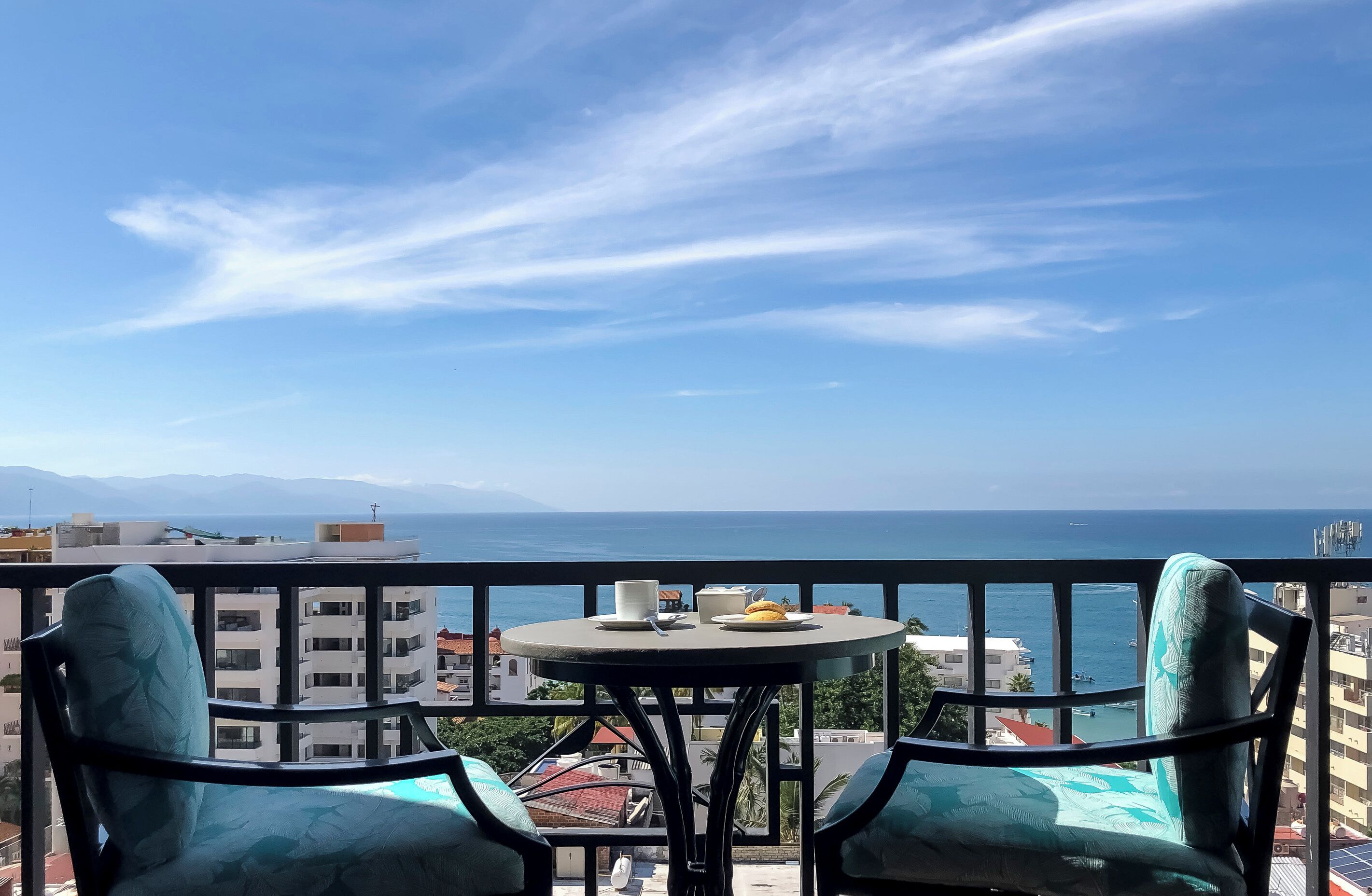 Un balcon avec deux chaises et une petite table, d’où l’on peut admirer le paysage urbain et la mer.