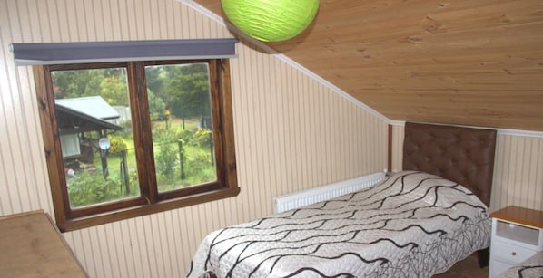 A bedroom with a bed, a window, a radiator, and a wooden ceiling. - El Refugio de la Cuenca (Puerto Octay)