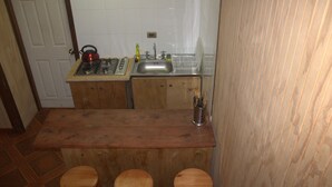 A small kitchen with a wooden countertop, a gas stove, a sink, and two stools. - El Refugio de la Cuenca (Puerto Octay)