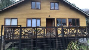 A two-story wooden house with a gabled roof, a front door, and a small porch area. - El Refugio de la Cuenca (Puerto Octay)